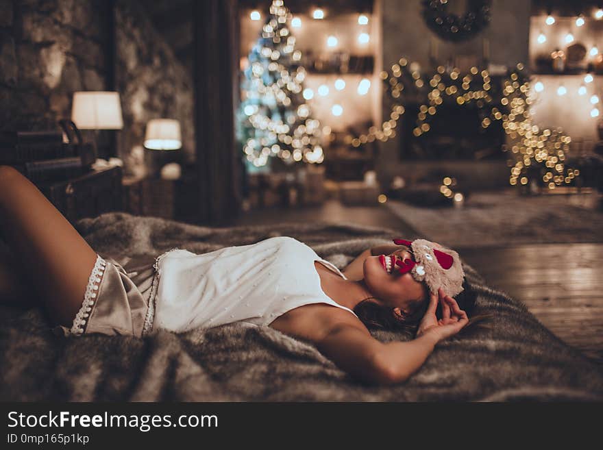 Beautiful asian woman is lying in bed and wearing sleeping mask at home near christmas tree in cozy interior. Interior