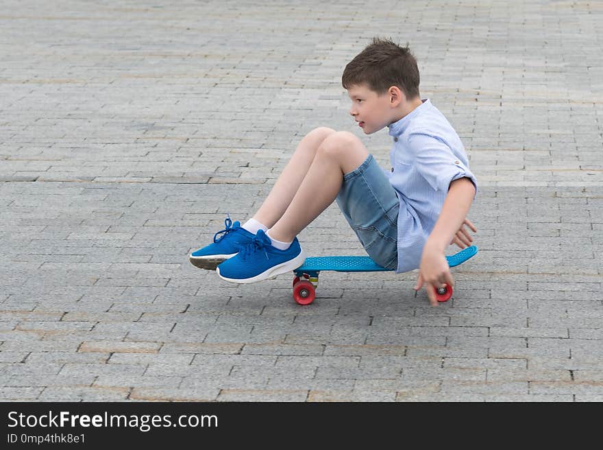 Boy riding on a blue skateboard on the road in a city park