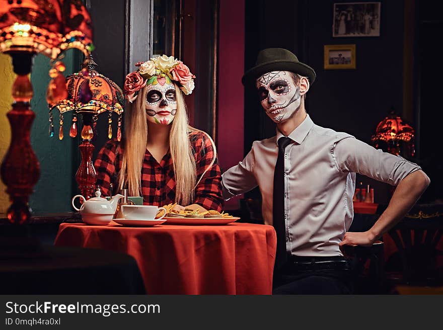 Halloween and Muertos concept. Young attractive couple with undead makeup ordered nachos during dating at a mexican restaurant. Halloween and Muertos concept. Young attractive couple with undead makeup ordered nachos during dating at a mexican restaurant.