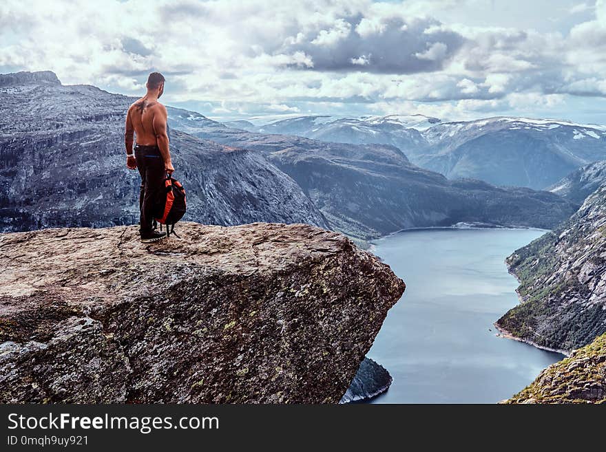 Tourist man standing in the Trolltunga and enjoys a beautiful view of the Norwegian fjord.