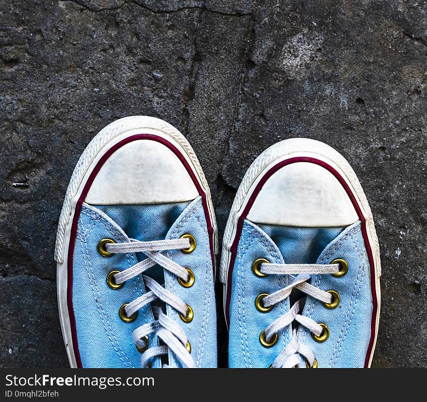 Pair of old worn blue textile sneakers on gray asphalt, top view