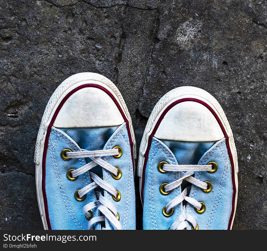 Pair of old worn blue textile sneakers on gray asphalt