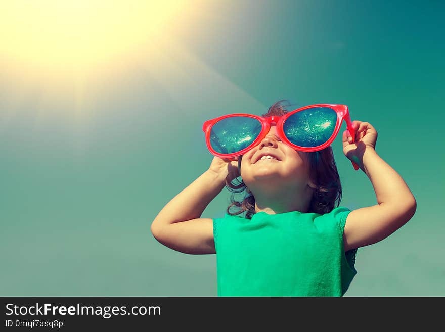 Happy little girl with big sunglasses looking at the sun