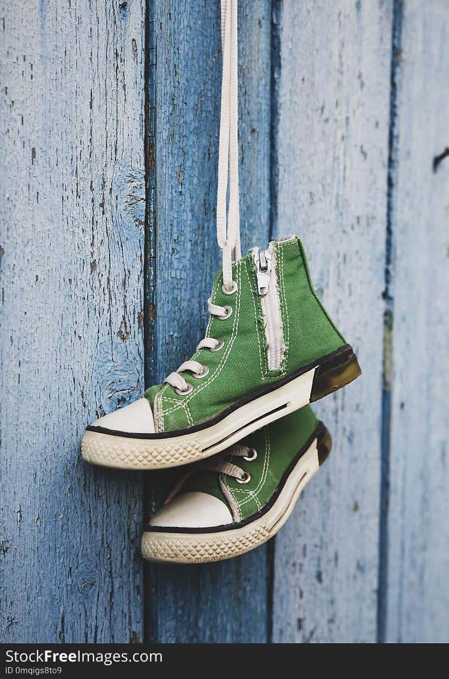 Pairs of old textile children`s green classic sneakers hang on a cord, blue shabby wooden background