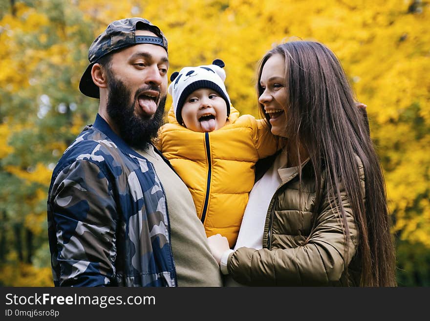 Happy family having fun outdoor. Close up portrait. Father, mother and daughter shows tongue. Autumn walk in the park