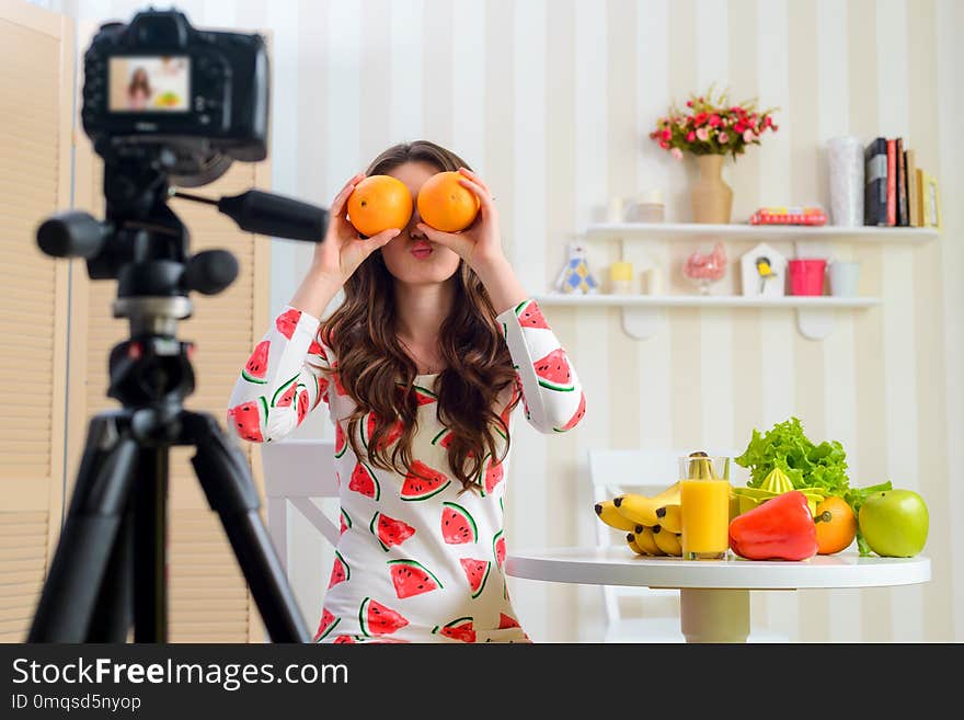 Woman playing with two oranges. Young female blogger is making a funny and foolish thing for her new video and standing near the table with a lot of fruits and vegetables.