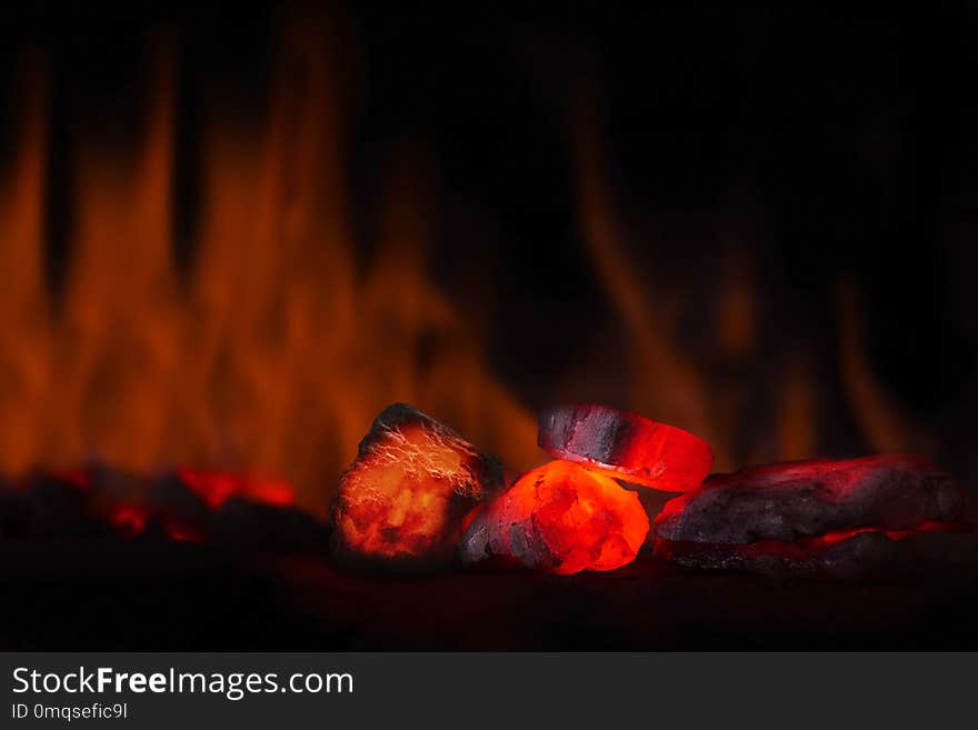 Red hot coal nugget in focus on dark background with flames. Background of raw coals with soft focus exclusion with color and temperature.