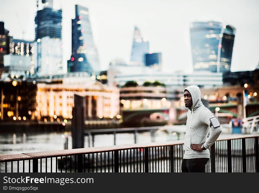 Young sporty black man runner with smartwatch, earphones and smartphone in an armband on the bridge in a city, resting. Copy space. Young sporty black man runner with smartwatch, earphones and smartphone in an armband on the bridge in a city, resting. Copy space.