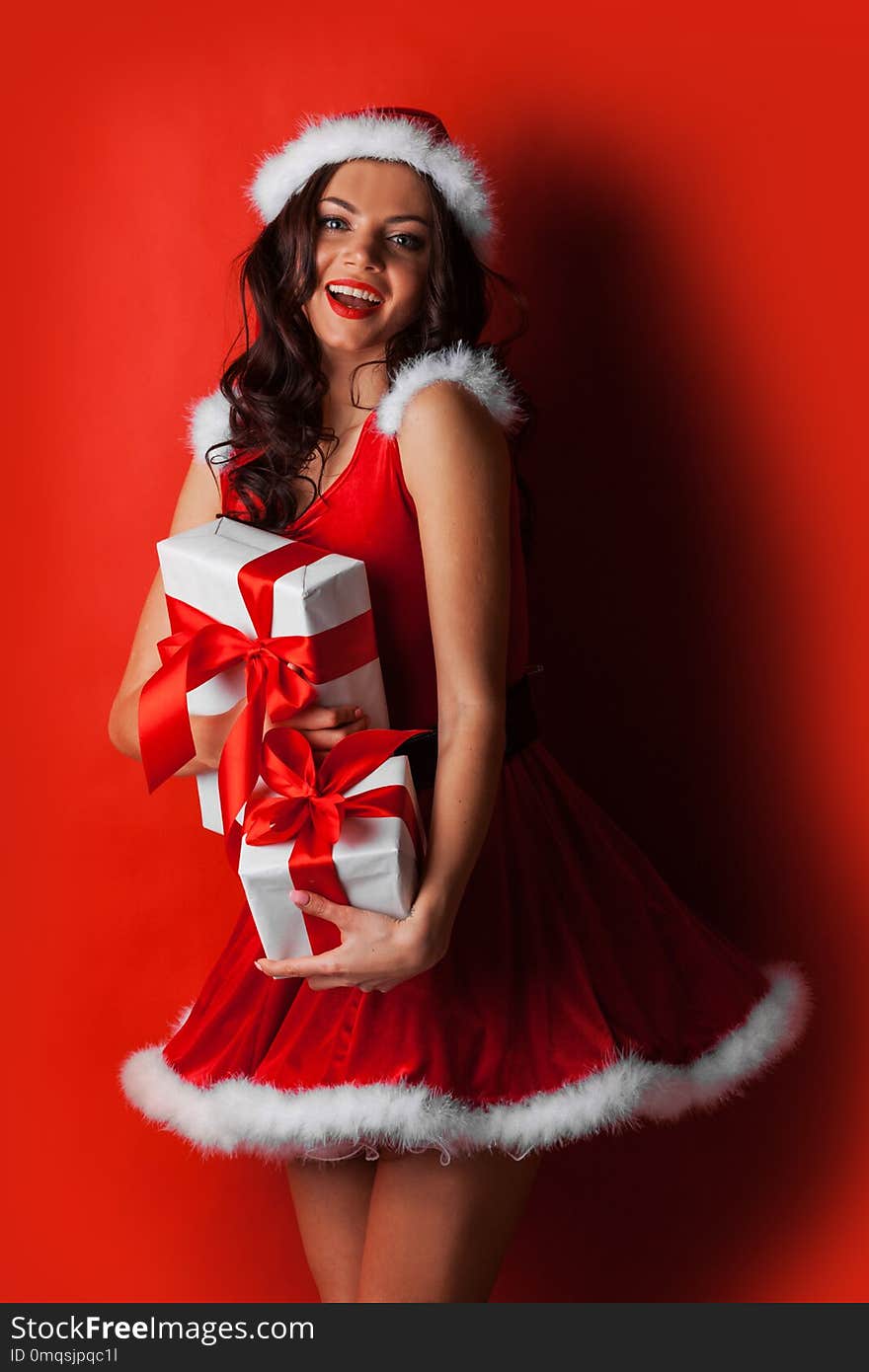 Pretty Pin-up style Santa girl in red hat and dress holding stack of gifts on red background. Pretty Pin-up style Santa girl in red hat and dress holding stack of gifts on red background