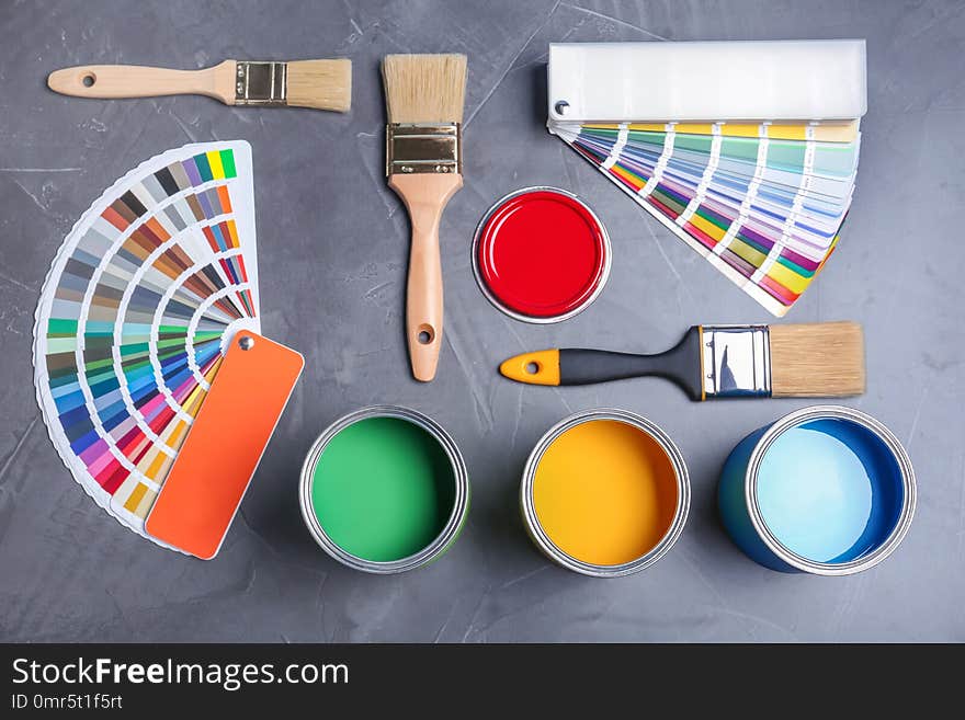 Flat lay composition with cans of paint, brushes and color palette samples on gray background