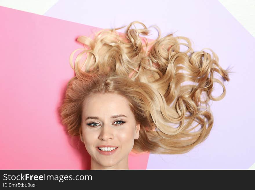 Beautiful woman with healthy long blonde hair on color background, top view