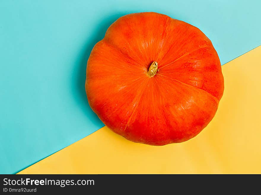 Beautiful orange pumpkin on colorful yellow and blue background, top view. Flat lay. Autumn, Halloween, harvest and holiday concept