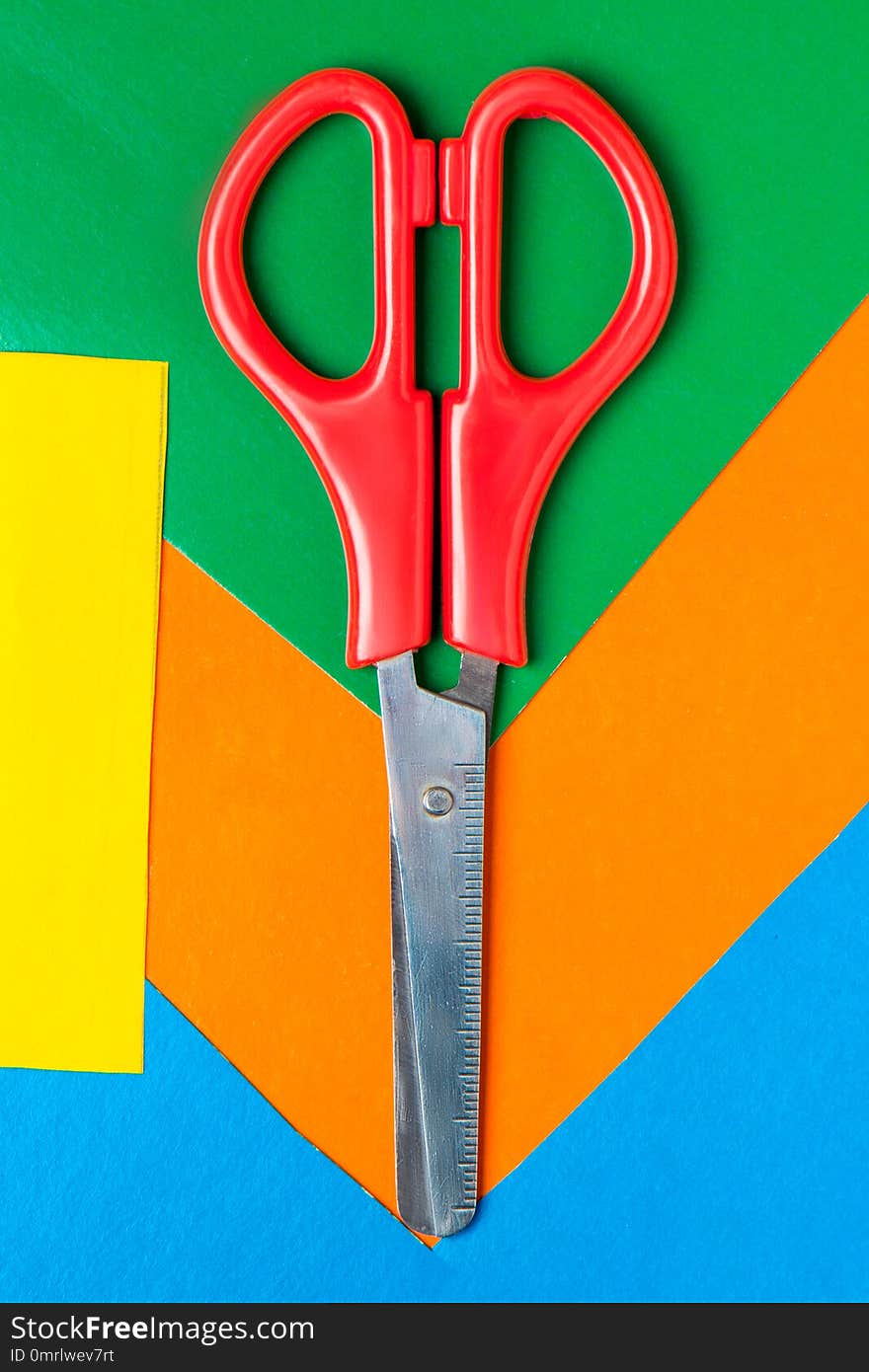 Scissors lie on multicolor paper. Green, Orange, Yellow, Blue