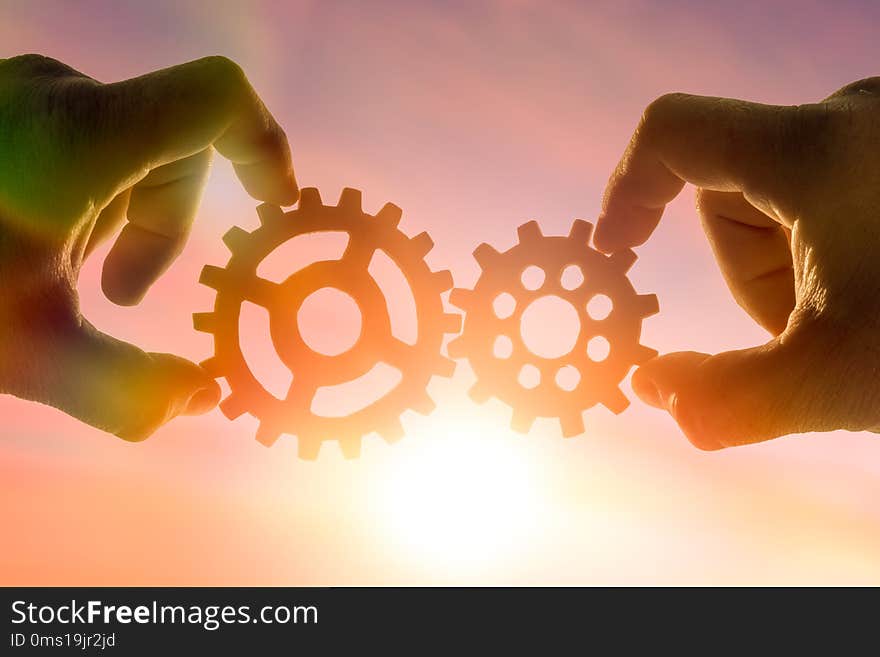 Hands businessman holding gears on the background of the sky in the sun, connecting the puzzle pieces. creation. mechanism. Business idea concept, teamwork, strategy, innovation, cooperation