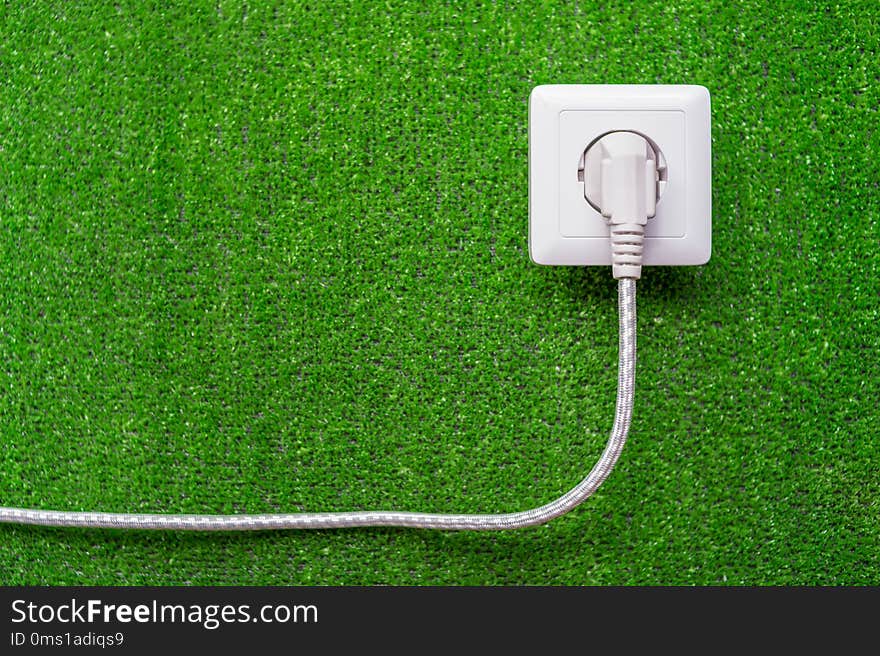 Concept of ecological reception of an electricity. Electric socket and plug with a cord on a background of green grass