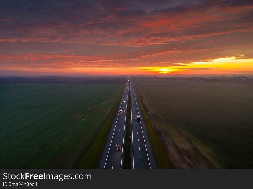 Road with cars under dramatic red sky in the morning. Transportation background. Aerial landscape. Autumn industrial morning.