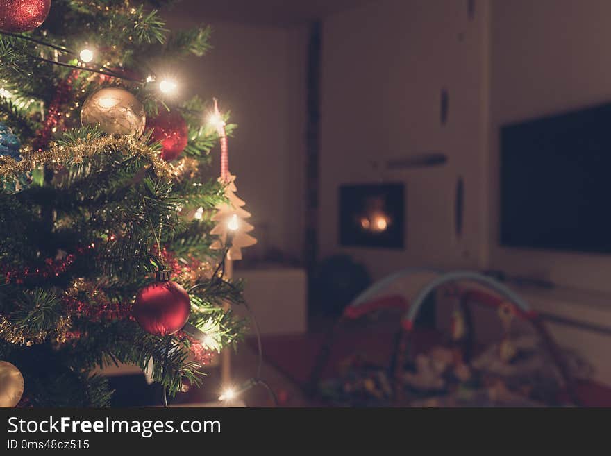 Retro image of decorated Christmas tree with lights indoors in living room with fire place and baby playground.