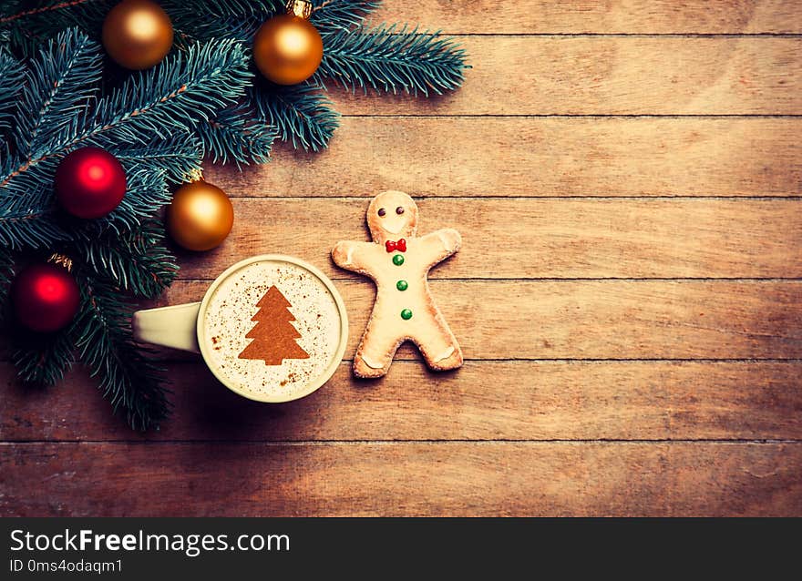 Cappuccino with gingerbread man and pine branch on wooden table.