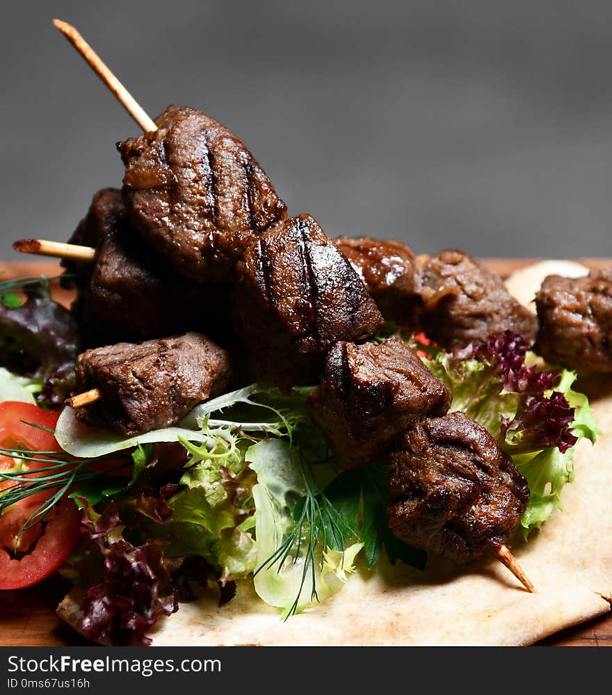 Tasty barbecue beef shashlik on wood plate with fresh vegetables and steam smoke on black background