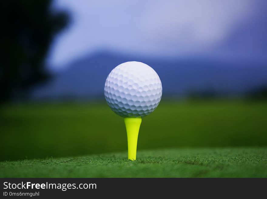 Golf ball on tee in beautiful golf course at sunset background.