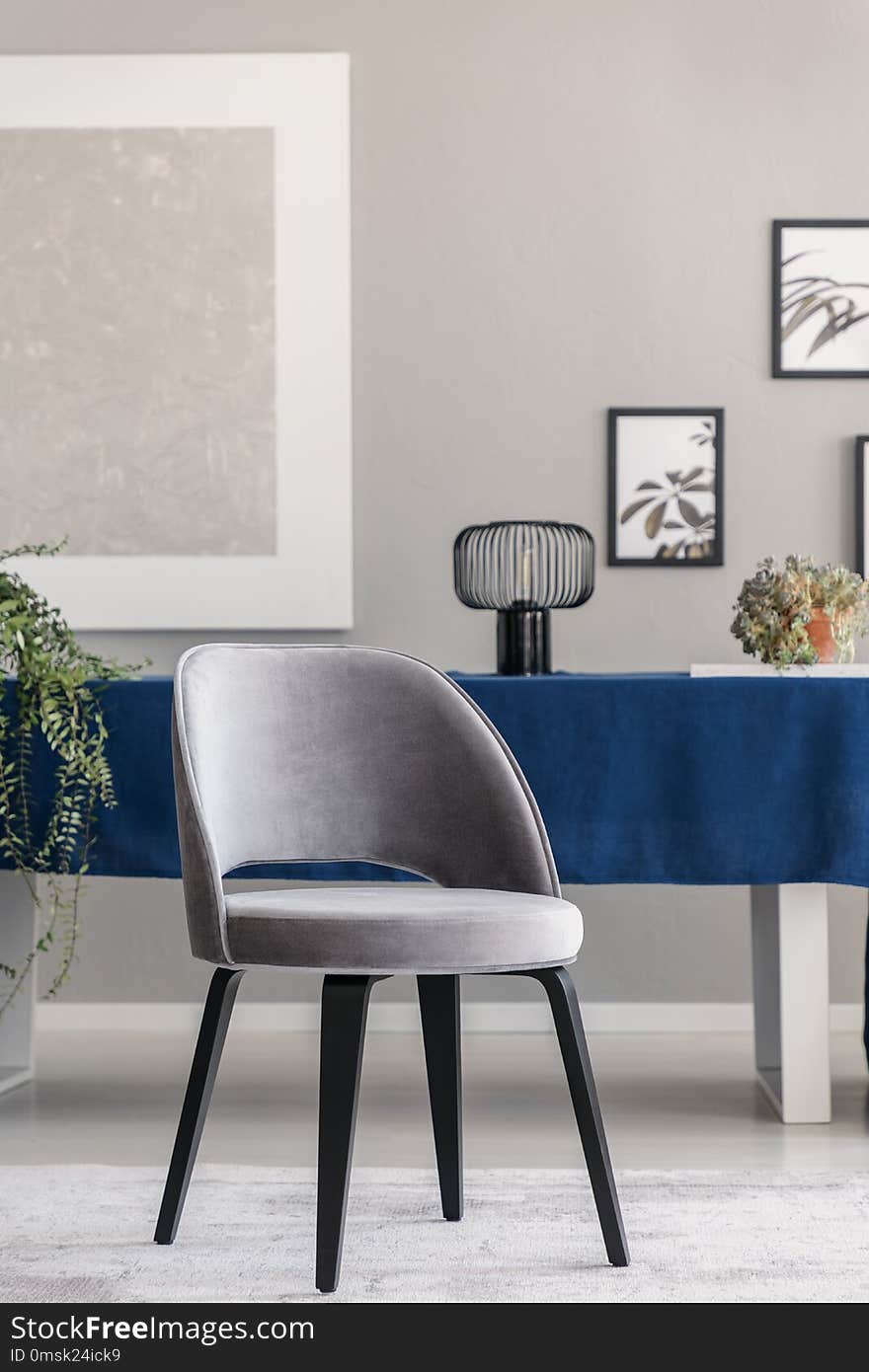 Modern chair at table with blue cloth in grey dining room interior with posters and lam