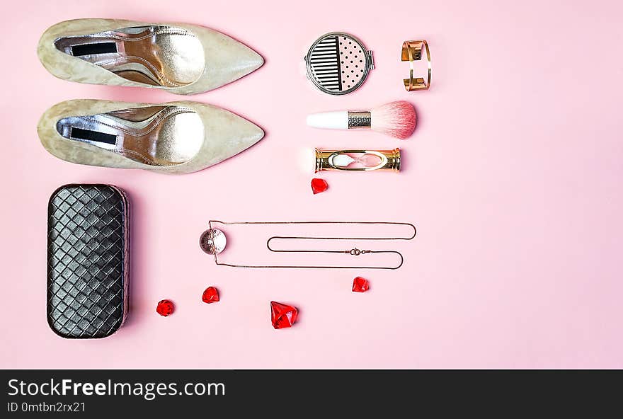 Fashion woman accessories outfit set gold colored heels jewelry clutch makeup cosmetic brushes pastel pink background. Flat lay top view copy space. Christmas New Year Valentines party conception. Fashion woman accessories outfit set gold colored heels jewelry clutch makeup cosmetic brushes pastel pink background. Flat lay top view copy space. Christmas New Year Valentines party conception.