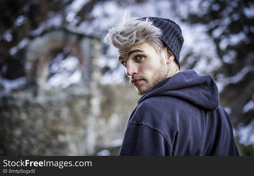 Portrait of young man in hoodie posing outdoor in winter setting with snow all around, looking at camera. Portrait of young man in hoodie posing outdoor in winter setting with snow all around, looking at camera.