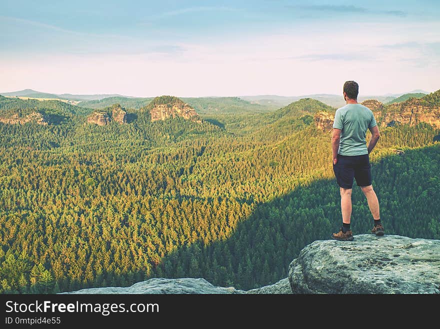 Tall man in outdoor clothes stands alone on the peak of rock.