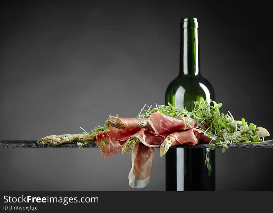 Asparagus wrapped in prosciutto with red wine on a dark background. Asparagus wrapped in prosciutto with red wine on a dark background.