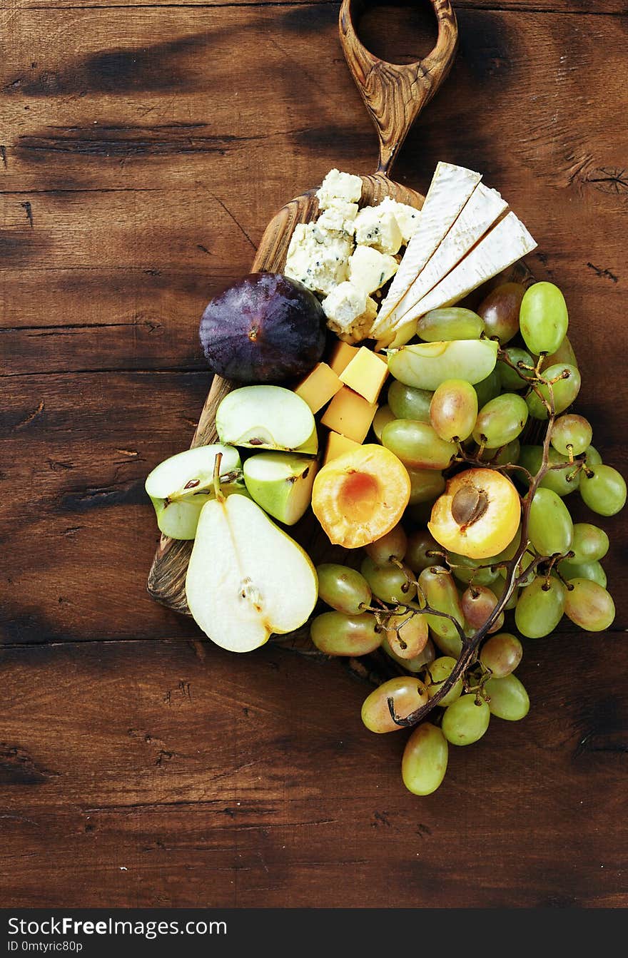 Top view flat lay appetizers table Various snacks: grapes, peach, apricot, pear, apples, hard cheese, brie cheese and roquefort cheese on wooden table. Top view flat lay appetizers table Various snacks: grapes, peach, apricot, pear, apples, hard cheese, brie cheese and roquefort cheese on wooden table