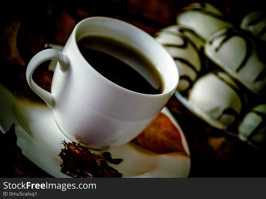 White cup and saucer with tea or coffee is on the table, autumn orange leaves