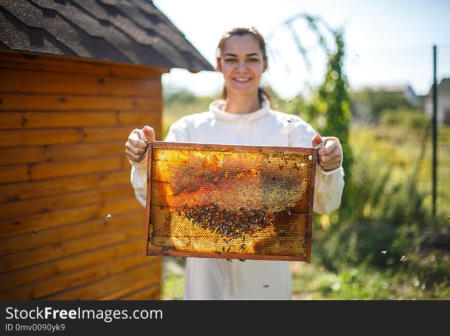 Young female beekeeper hold wooden frame with honeycomb. Collect honey. Beekeeping concept.