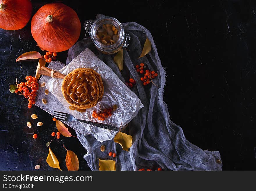 Autumn concept. Pumpkin pancakes with caramel topping, with pumpkins, leaves on a dark background. Top view Copy space