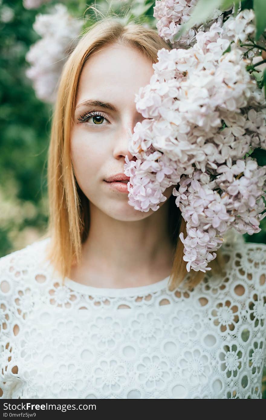 Beautiful attractive young woman posing in spring syringa park wearing white knitted top and blue jeans, modern creative toning