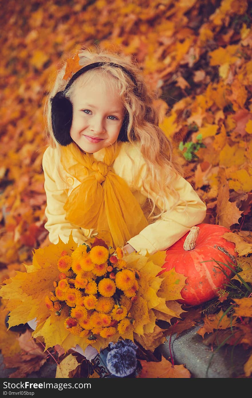 Little beautiful blond girl with big pumpkin in autumn background