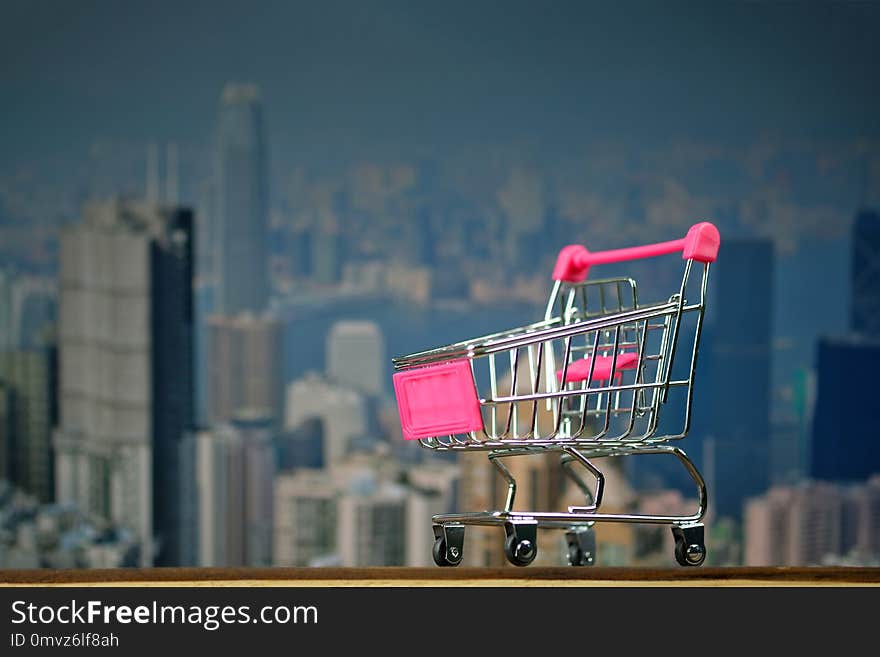 Shopping cart or supermarket trolley on top wooden working table with city and office building background, business and financial concept idea.