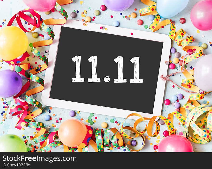 11.11 on a school slate with colorful carnival frame of multicolored balloons, confetti, candy and twirled streamers in a conceptual image. 11.11 on a school slate with colorful carnival frame of multicolored balloons, confetti, candy and twirled streamers in a conceptual image