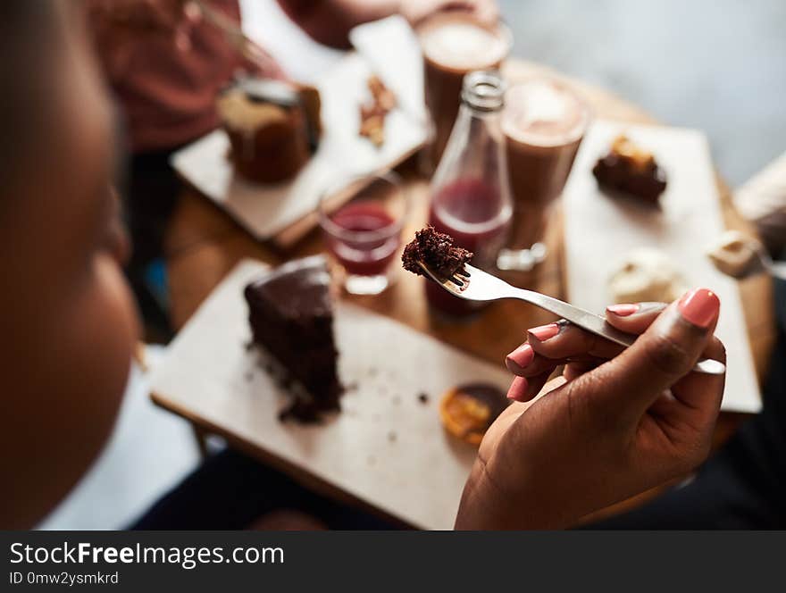 Young woman eating a piece of chocolate cake with a fork while sitting at a cafe table with a group of friends. Young woman eating a piece of chocolate cake with a fork while sitting at a cafe table with a group of friends