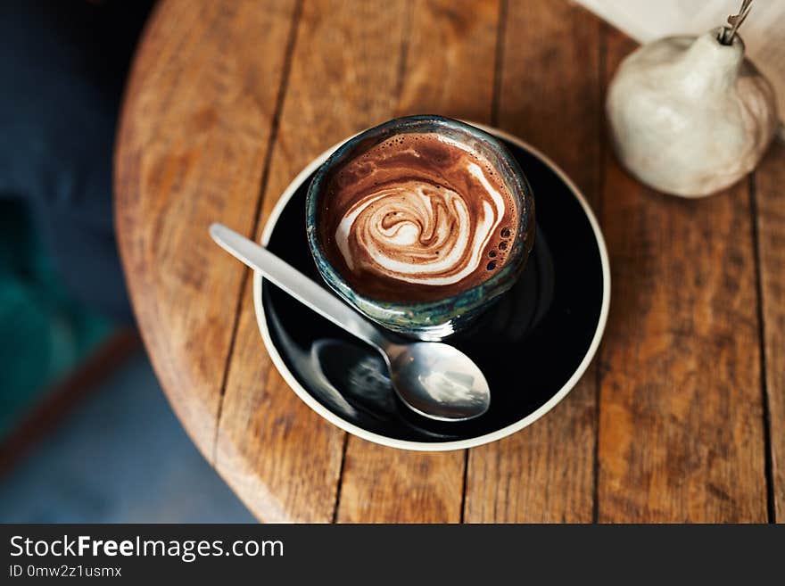 High angle of a delicious latte sitting with a spoon on a wooden table in a cafe. High angle of a delicious latte sitting with a spoon on a wooden table in a cafe