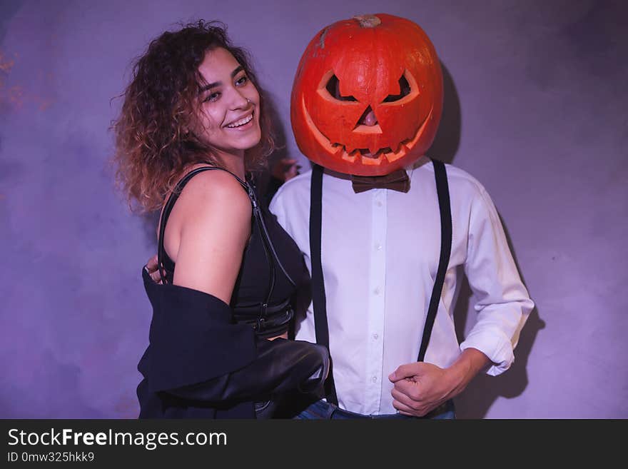 Unusual couple at the Halloween party. Man with carved pumpkin on his head and funny women near pumpkin boy. Unusual couple at the Halloween party. Man with carved pumpkin on his head and funny women near pumpkin boy