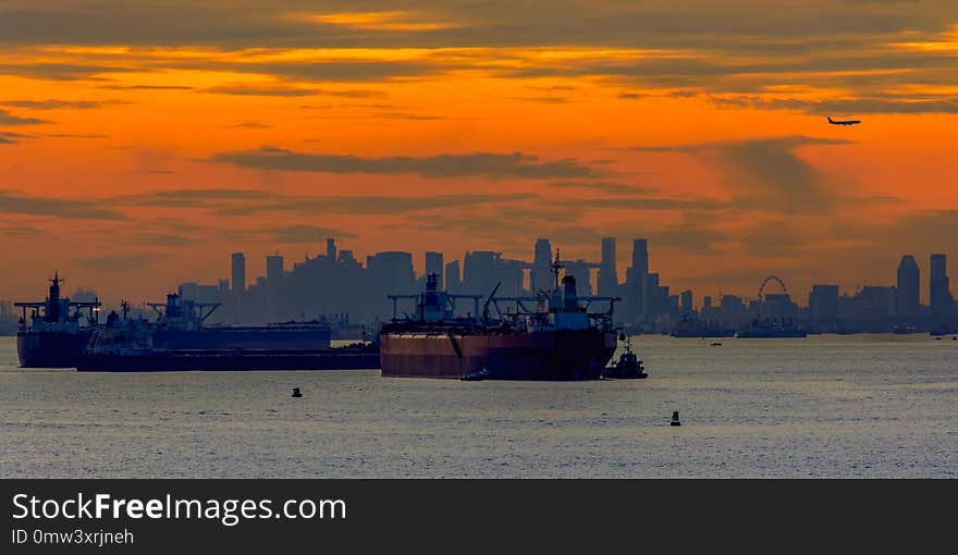 Sunset over Singapore strait with landing airplane and anchored oil tankers and others ship