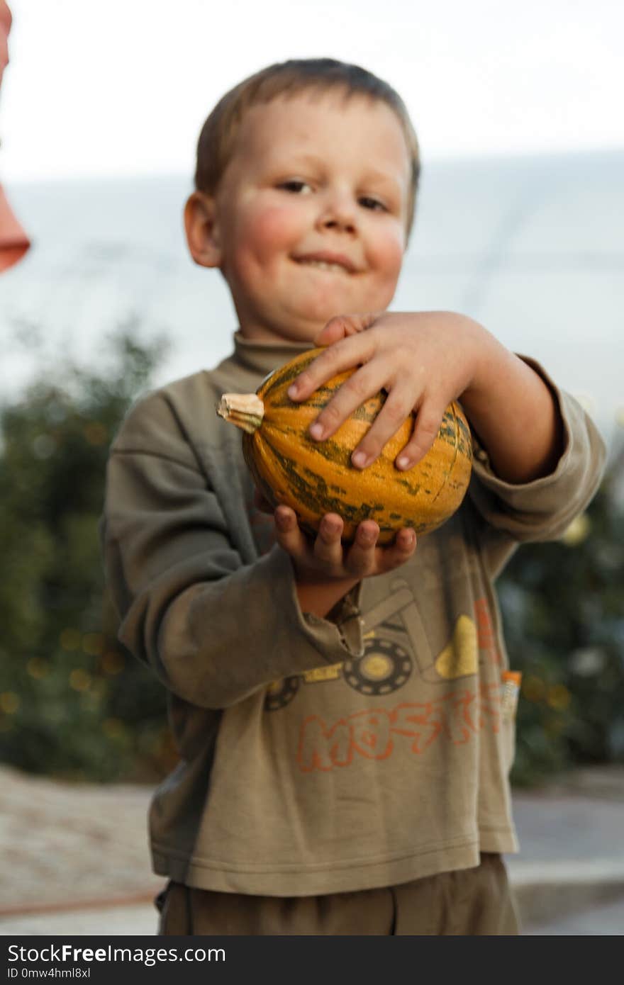 Smiling boy standing with big yellow pumpkin in hands