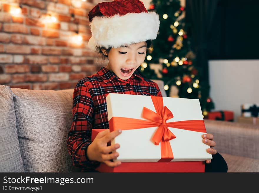 Joyful cute little girl surprised open christmas gift at home. attractive girl childhood with santa hat sitting in living room. open gifts boxing day concept.