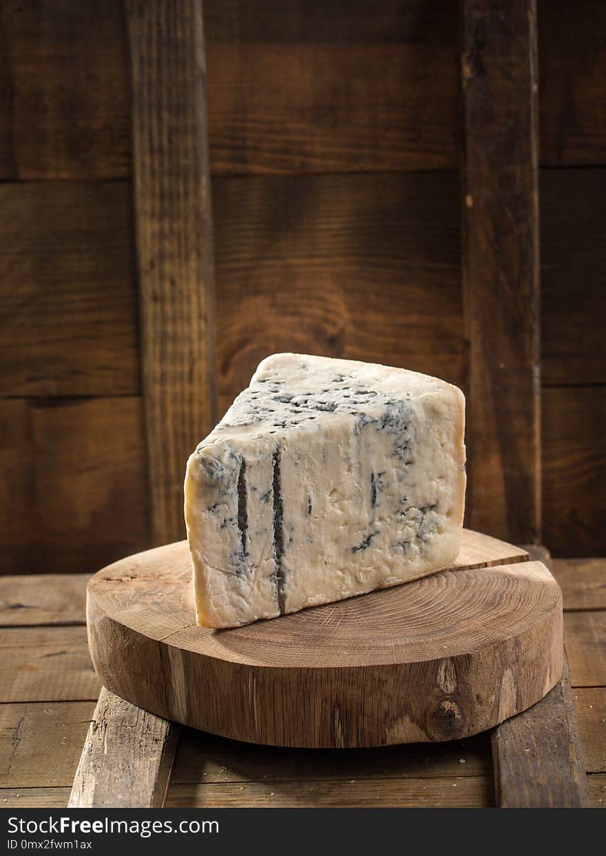 Slice of blue cheese on wooden board on dark background. Studio shot