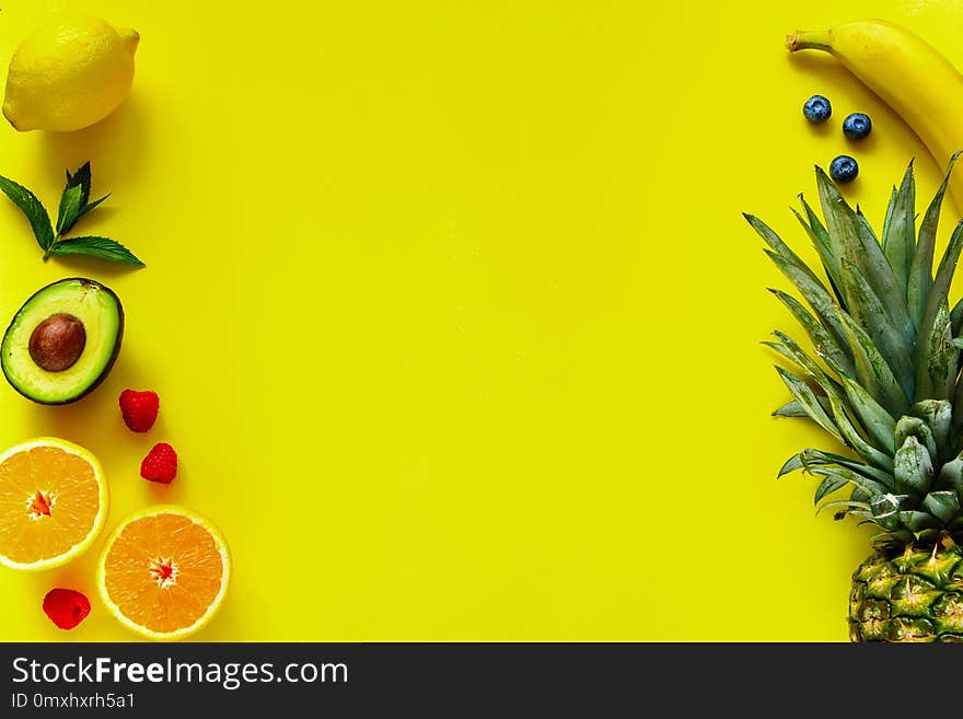 Creative layout made of various tropical fruits on yellow background. Pineapple, banana, orange, lemon, avocado, raspberry, blueberry. Food concept. Flat lay, top view