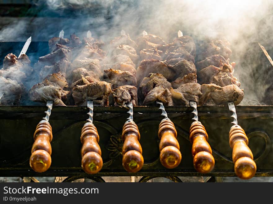 Grilled meat, Golden pork with skewers and wooden handles. A lot of smoke in the process of cooking fragrant meat dishes in nature. Summer kitchen. Raw meat on fire.