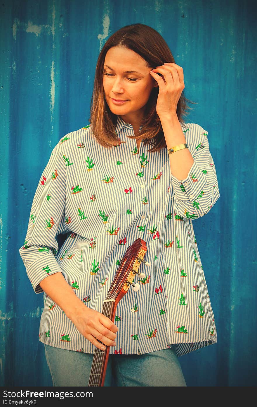 Fashion. Portrait of a beautiful smiling woman with a guitar near a bright blue fence. Street musician. image filter retro style