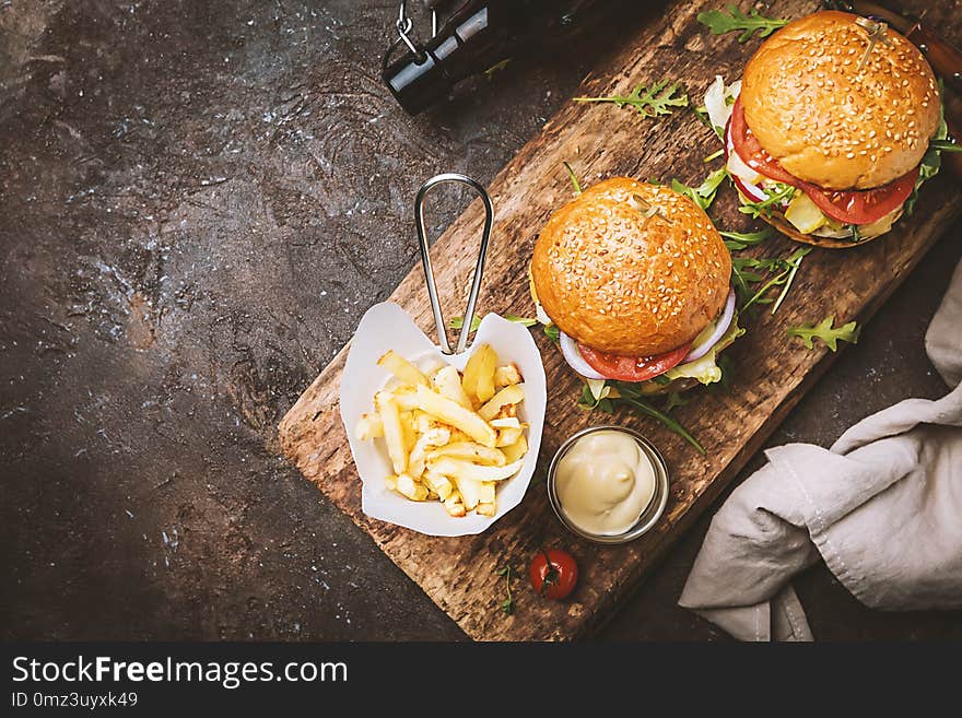 Two tasty grilled classic beef burgers with French fries on a rustic black table, top view with copy space