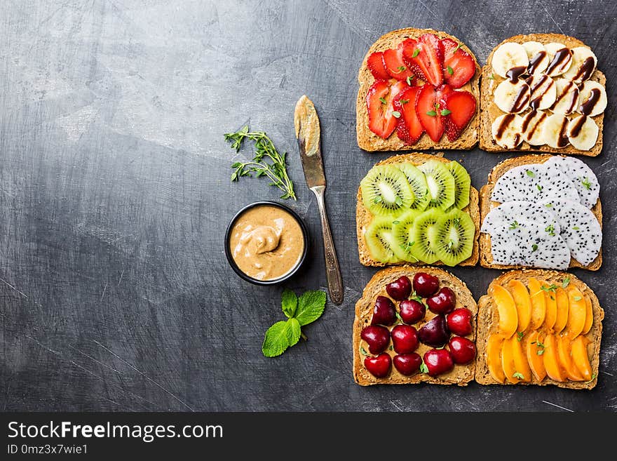 Traditional American and European summer breakfast: sandwiches of toast with peanut butter, berries and fruits peach, strawberry, banana, cherry, kiwi and dragon fruit, top view