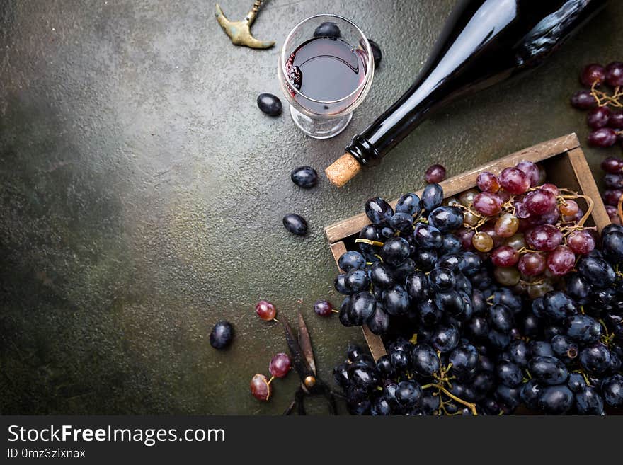 A bottle of red wine with glass and grapes over dark stone background, copy space , top view. A bottle of red wine with glass and grapes over dark stone background, copy space , top view.